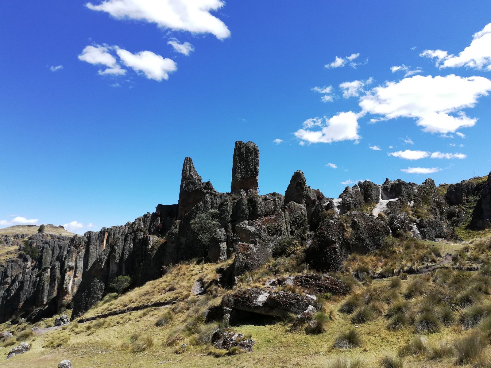 Formaciones de roca gris y afilada sobre un cerro de pasto, bajo un cielo azul con nubes blancas