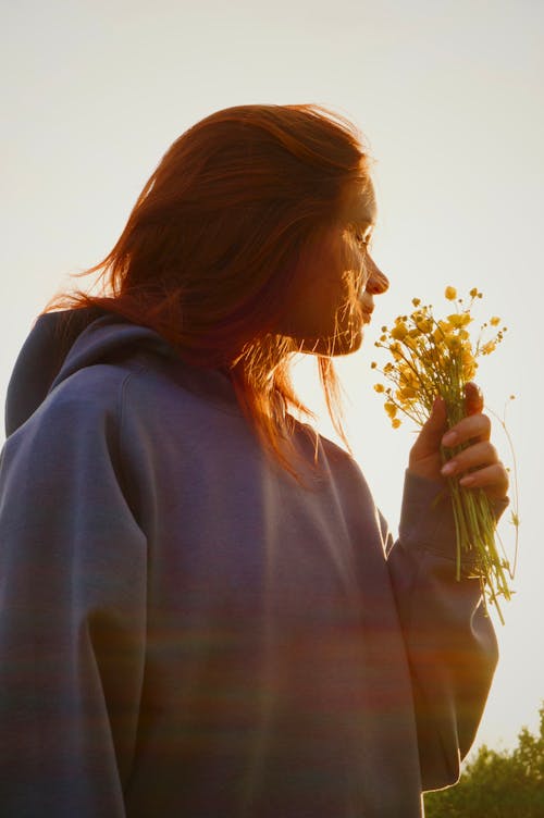 Portrait of Woman in Hoodie Smelling Flowers