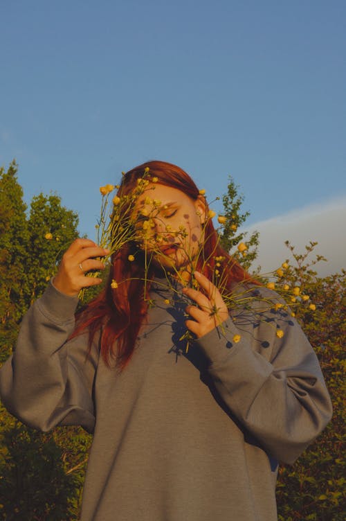Posed Photo of a Red-Haired Woman Covering Her Face with Flowers