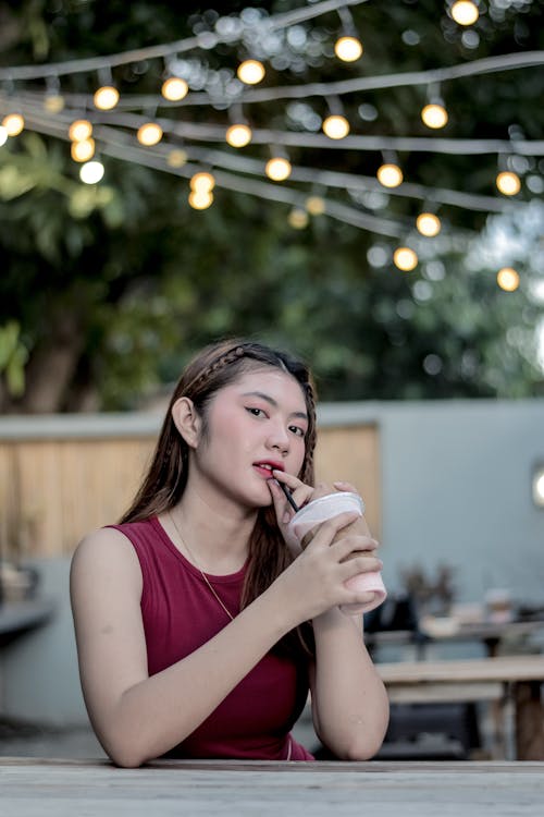 A Woman in Red Sexy Top Sipping Cold Drink while Looking at the Camera