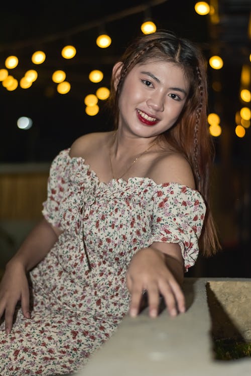 A Woman in Off-Shoulder Dress Leaning on a Concrete Railing while Smiling at the Camera