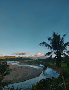 Breathtaking view of a river and mountains in Abuyog, Philippines with a palm tree foreground. - Fotografer Sidoarjo