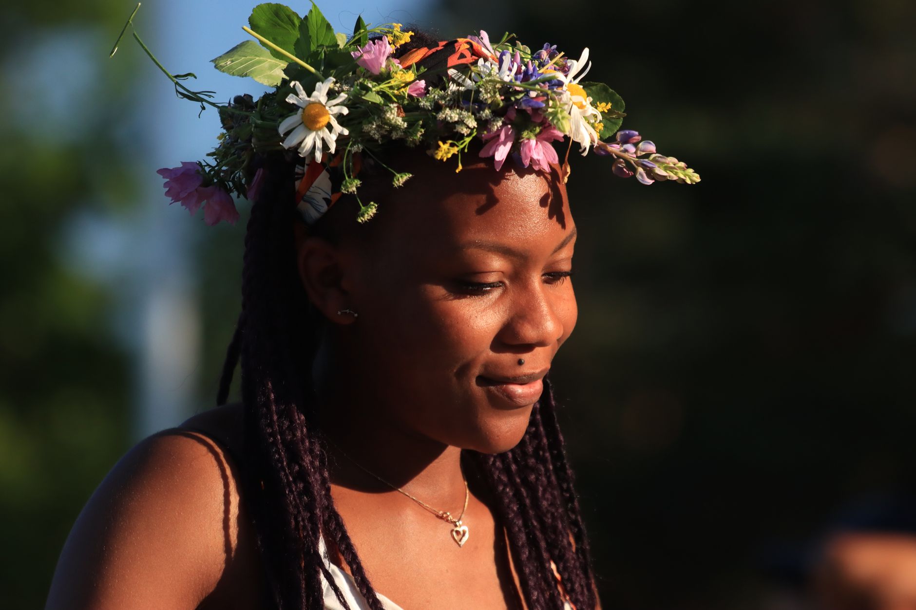 African American woman wearing a flower crown enjoys a sunny day outdoors.