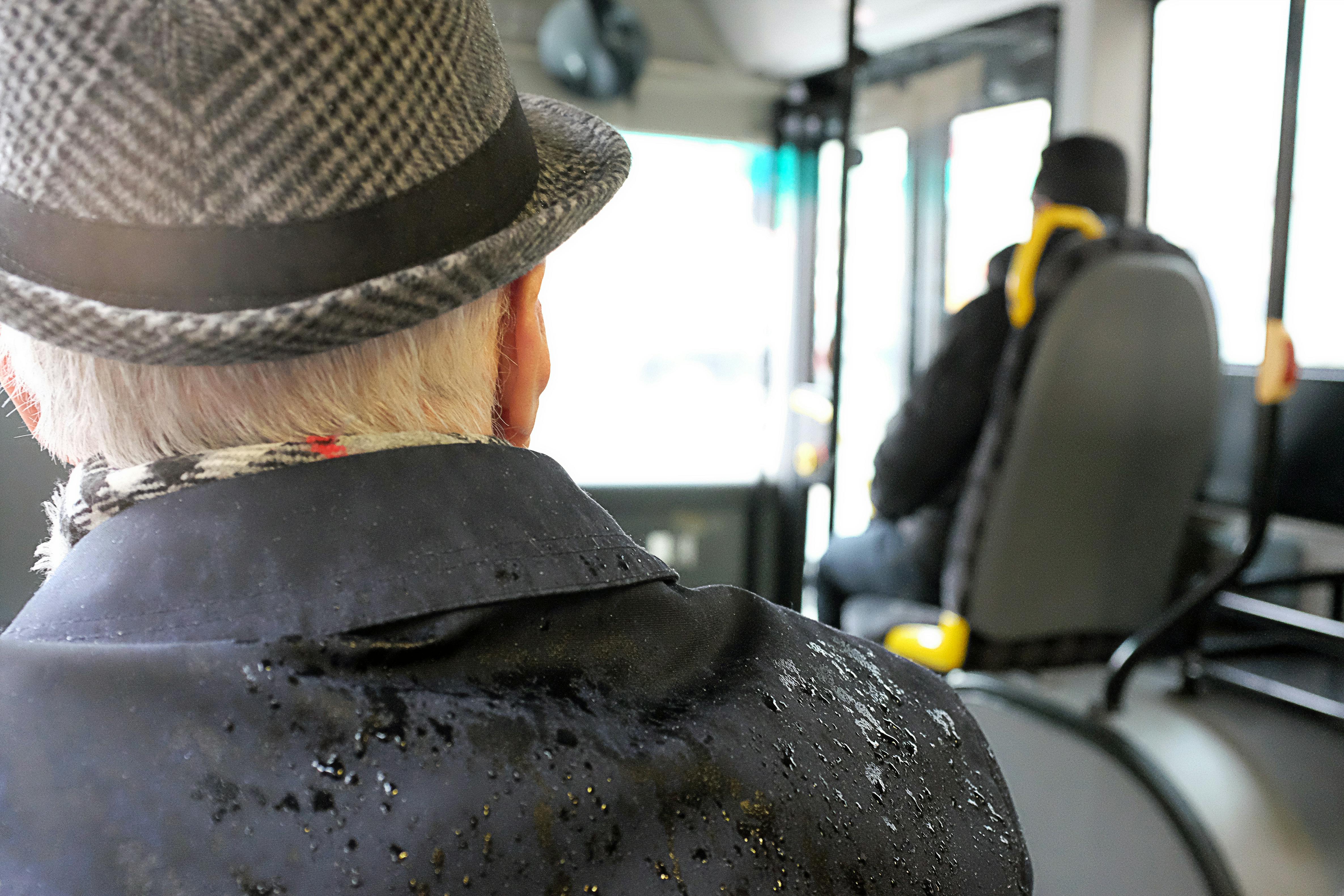 Senior man in a hat on a rainy day bus journey, reflecting travel mood.