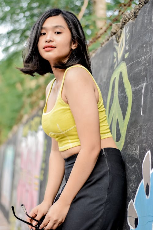 Girl in Yellow Crop Top Leaning on Concrete Wall