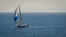 在晴朗的夏日天空下，一艘帆船滑过波光粼粼的蓝色海洋，这正是休闲与旅行的缩影