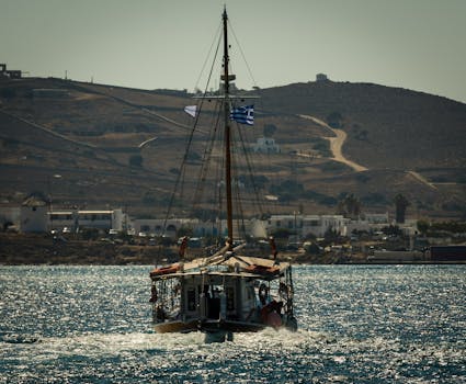 一艘悬挂希腊国旗的传统帆船，正航行在晴朗天空下的爱琴海上
