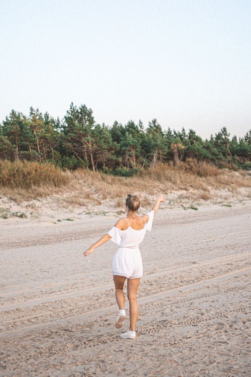Free Woman in a white outfit walking joyfully on Palanga beach during the day. Stock Photo