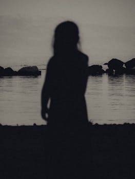 Silhouette of a woman standing by the sea at dusk in Corfu, Greece. Serene and moody atmosphere.