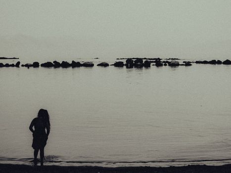 A serene silhouette of a woman by the calm seashore in Corfu, Greece, at twilight.