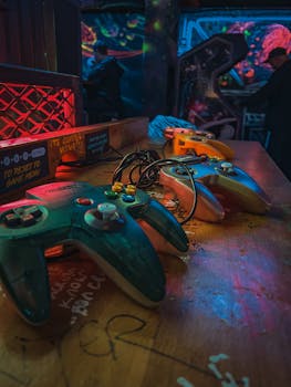 Close-up of vintage gaming controllers on a colorful wooden desk in an arcade setting.