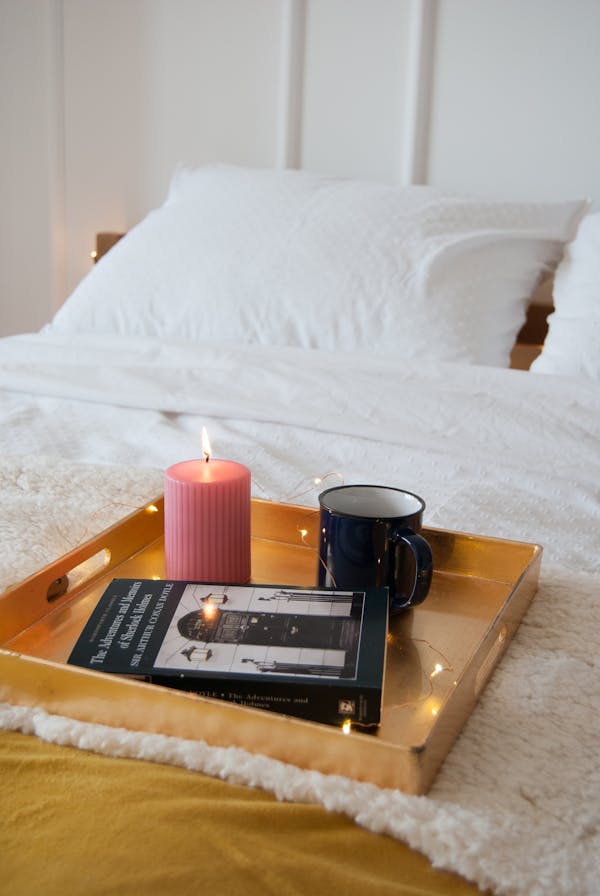 Bed table with a lighted pink candle, a mug of coffee, and a book for addiction treatment.