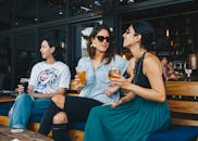 在热闹的户外酒吧里，三名女士正喝着酒