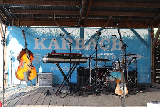 An outdoor stage with various musical instruments including a cello, drum set, and keyboard.