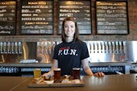 在一家提供精酿啤酒航班的酒吧里，微笑的调酒师站在水龙头和菜单板前