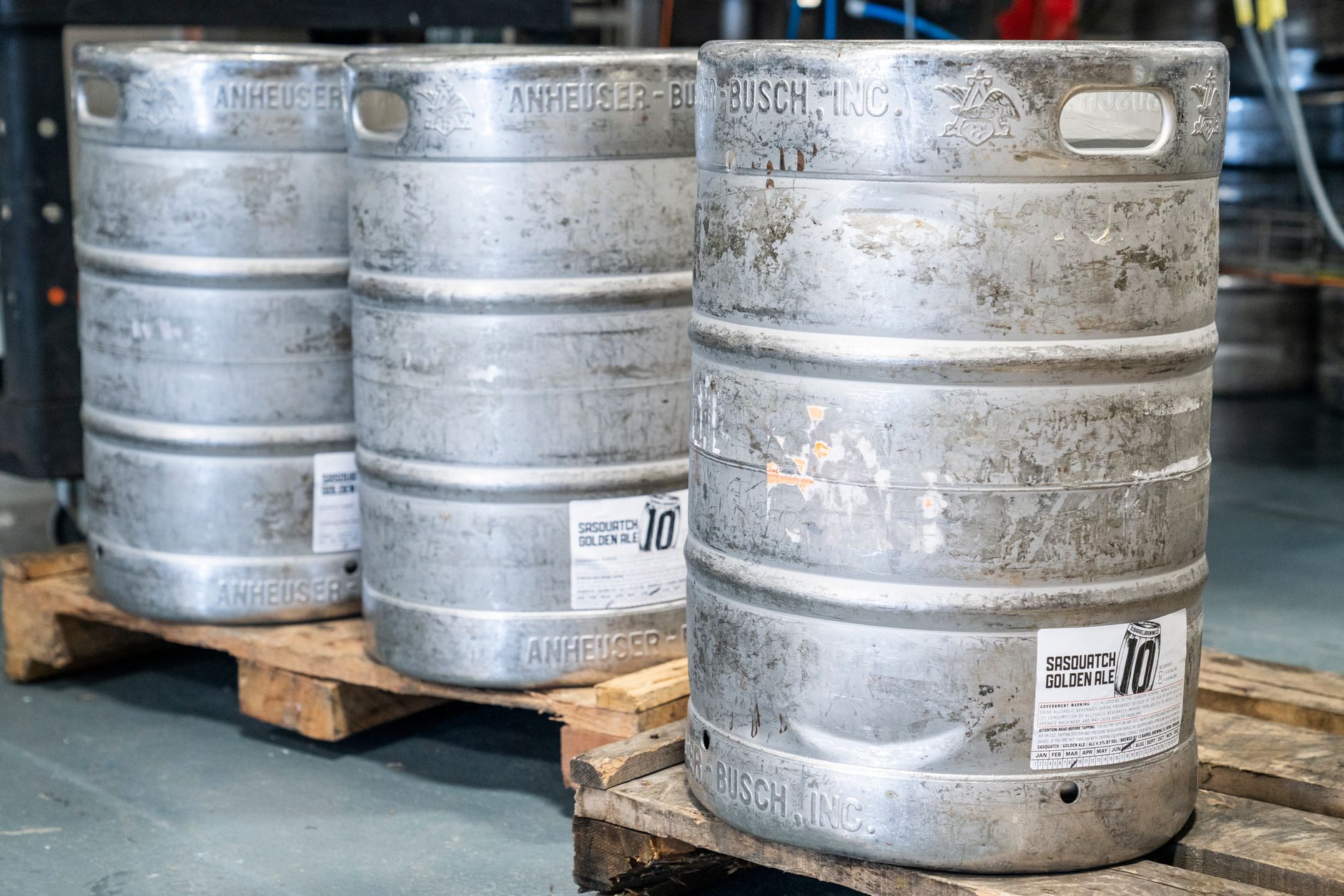 Image of metal beer kegs on wooden pallets in an indoor brewery setting, ideal for industrial storage themes.