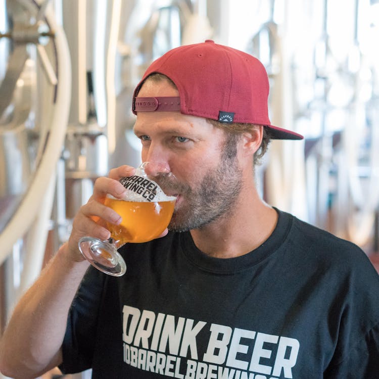 Man Drinking Liquor Wearing Red Cap And Black Crew-neck Shirt