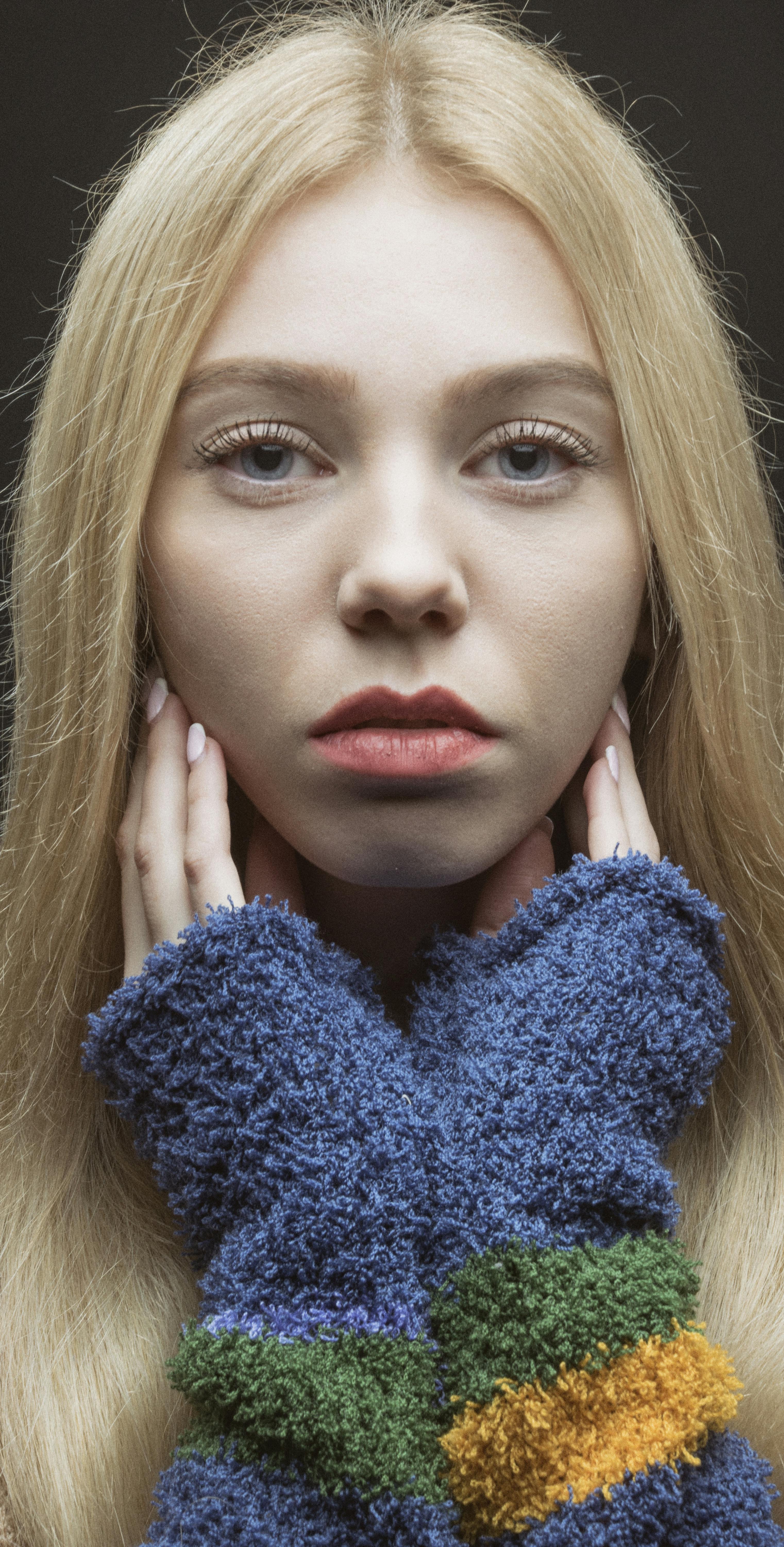 A striking close-up portrait of a young woman with blonde hair in a colorful knit sweater.