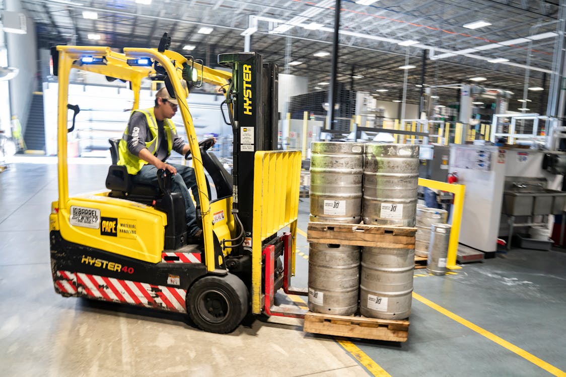 Free Person Driving Yellow Forklift Carrying Metal Barrels Stock Photo