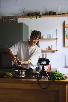 Man preparing food while recording a cooking vlog in a stylish kitchen setting.