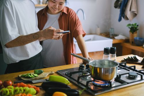 Free A couple cooking together and using a smartphone for recipes in a cozy kitchen. Stock Photo