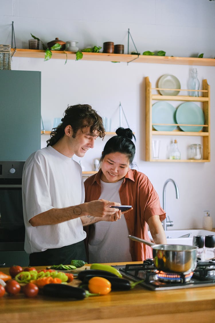 Couple Cooking And Looking At A Phone In A Kitchen