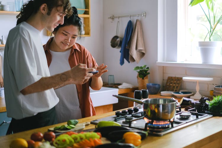 Couple Cooking And Looking At A Phone In A Kitchen