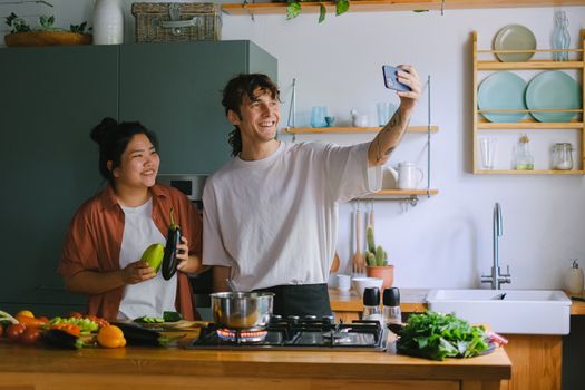 Happy couple cooking and taking a selfie in a modern kitchen with fresh vegetables.