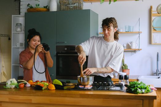 A couple engaged in cooking and photography in a modern kitchen setting.