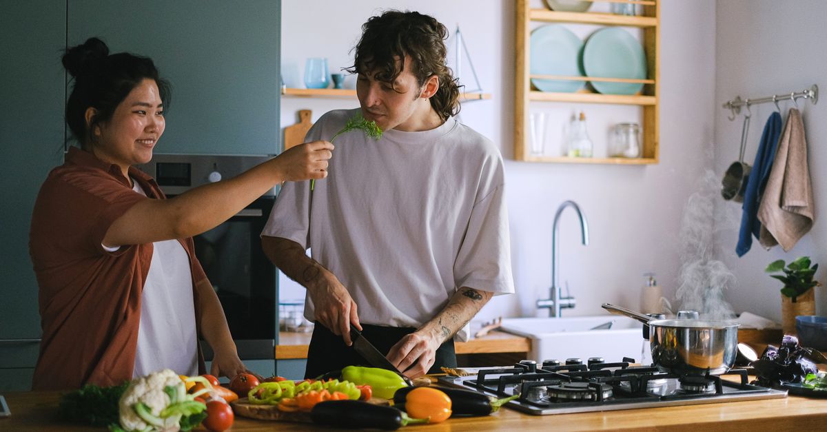 student cooking in a shared hostel kitchen with fresh vegetables and spices on the counter
