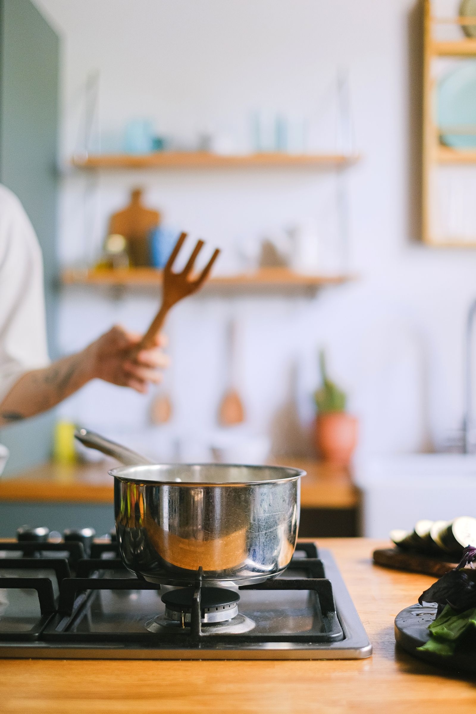 A cozy kitchen scene with a hand stirring in a stainless steel pot on a stove.