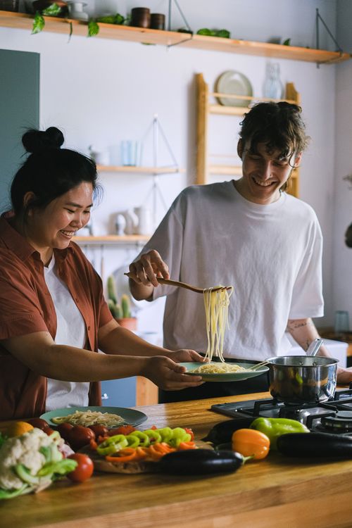 Free Smiling couple cooking pasta together in a cozy kitchen setting, enjoying a relaxed and fun meal preparation. Stock Photo