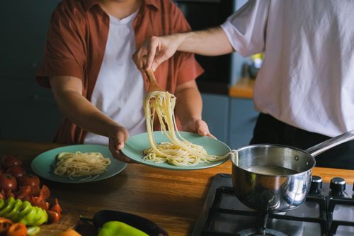 Free Two adults serving homemade spaghetti onto plates in a cozy kitchen setting. Stock Photo