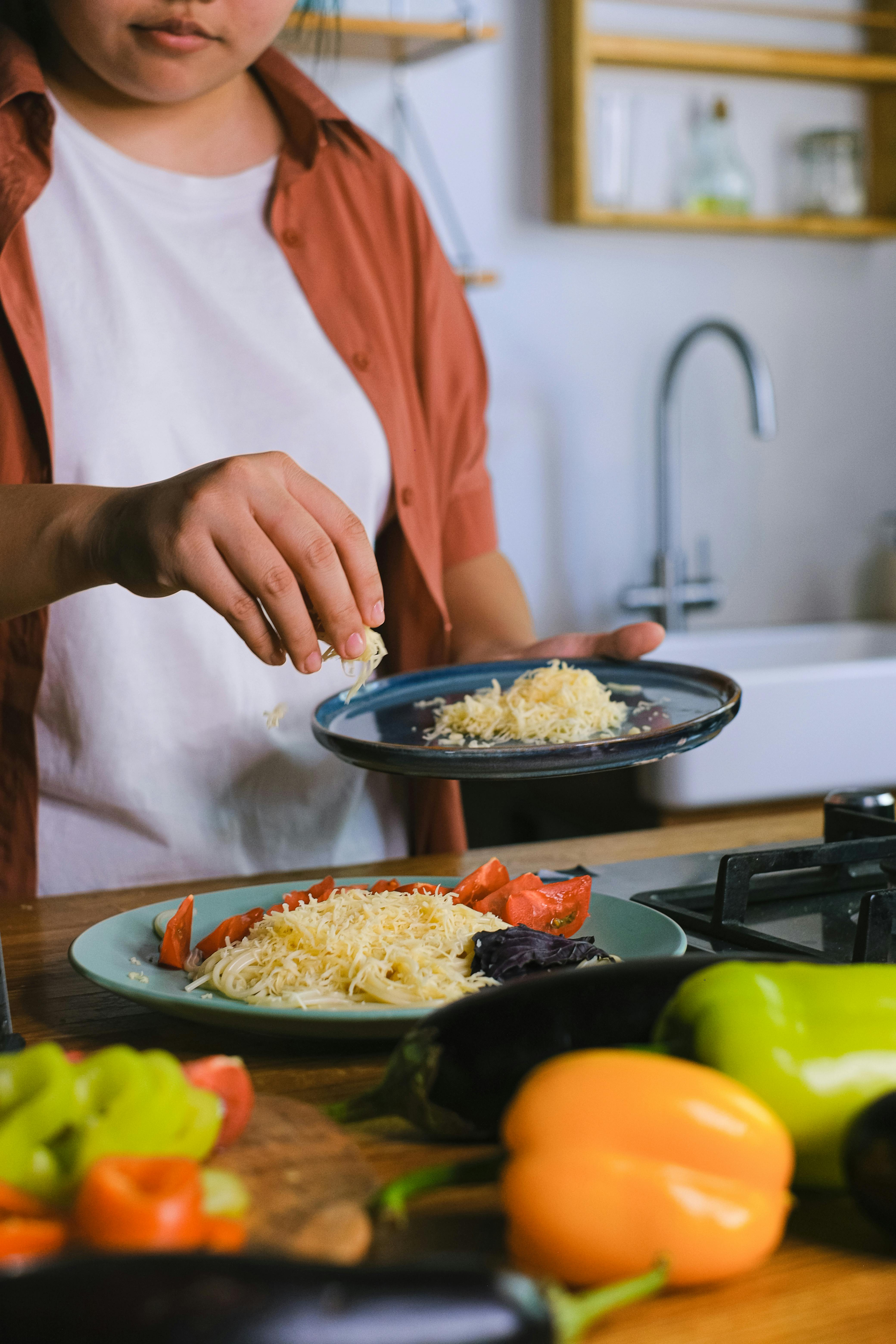 Person preparing pasta with grated cheese in a cozy kitchen space.