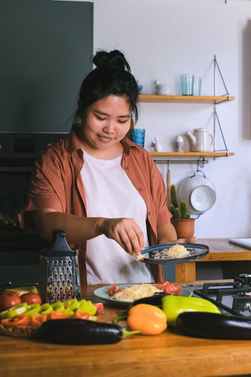 Free Woman in kitchen preparing a pasta dish with fresh ingredients, smiling and engaging in culinary activities. Stock Photo
