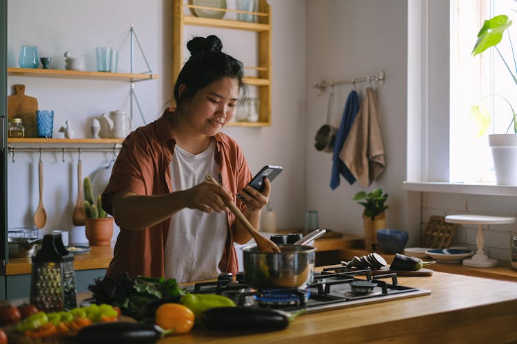 Woman Using A Phone While Cooking In A Kitchen