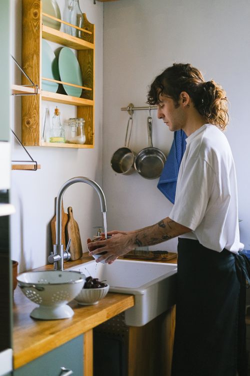 Free Young adult washing dishes in a cozy and modern kitchen setting, emphasizing home life and domesticity. Stock Photo