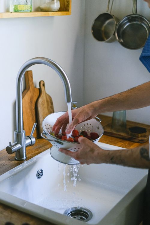 Free A person rinsing strawberries in a colander under running water in the kitchen. Stock Photo