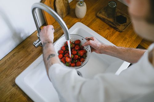 Free A person washes fresh strawberries in a kitchen sink using a strainer. Overhead angle captures the process. Stock Photo