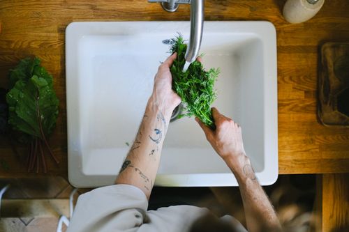 Free Tattooed hands washing fresh herbs in a kitchen sink, highlighting daily culinary routines. Stock Photo