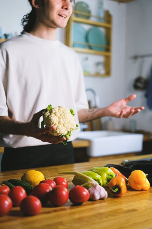 Free A man holds a cauliflower while preparing fresh vegetables in a modern kitchen. Stock Photo
