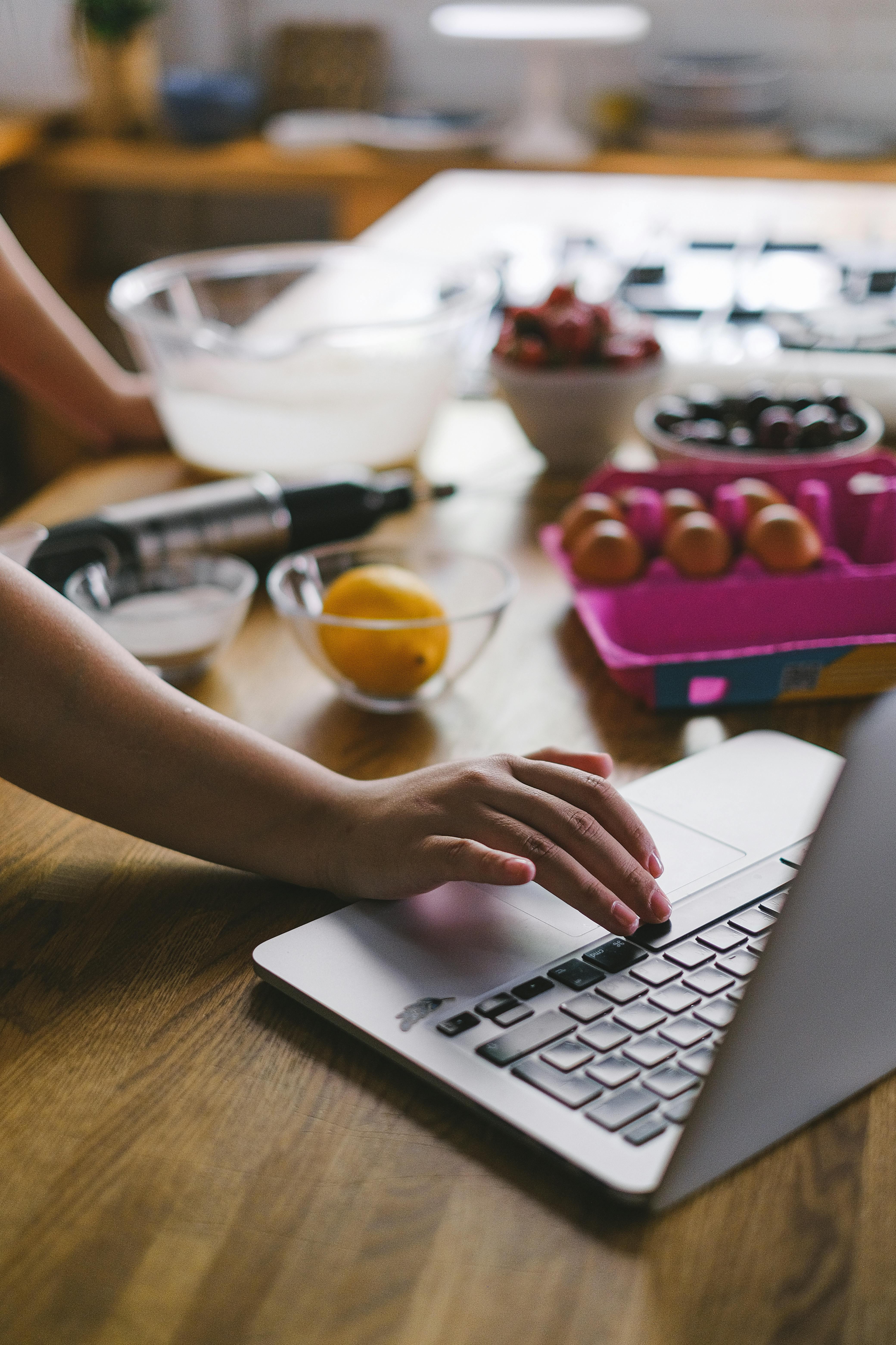 A close-up shot of someone typing on a laptop, with a cooking blog or recipe website on the screen.