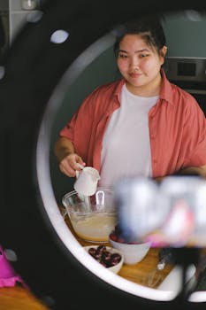 An Asian woman joyfully prepares food in a kitchen, surrounded by ingredients and kitchen tools.