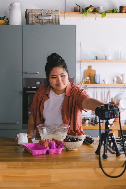Free A woman filming a cooking tutorial in a modern kitchen setting. Stock Photo