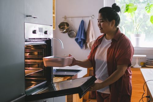 Free A woman prepares to bake by placing a dish in the oven in a sunny kitchen. Stock Photo