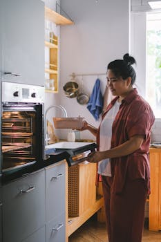 Woman placing a baking dish into an oven in a contemporary kitchen setting.