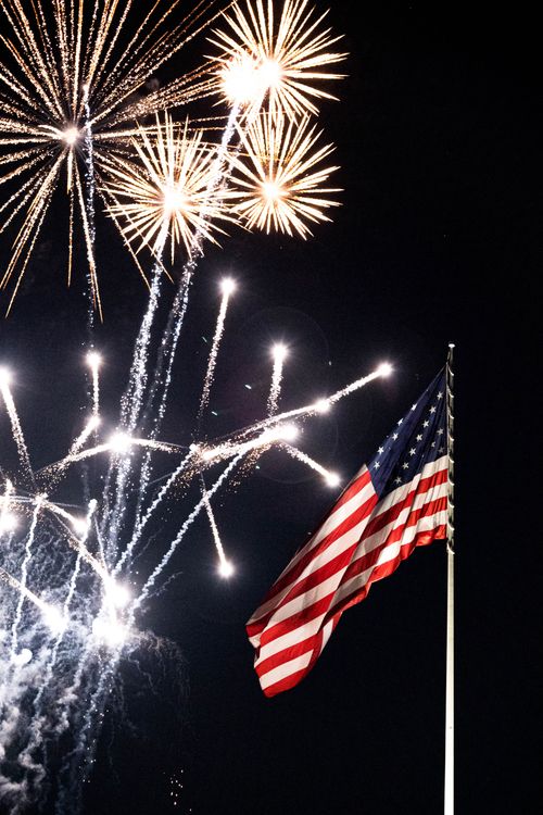 Free American flag waving with fireworks bursting in the night sky over New York. Stock Photo