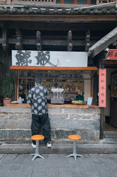 A bustling street food stall with a customer, vibrant signages, and cozy seating.