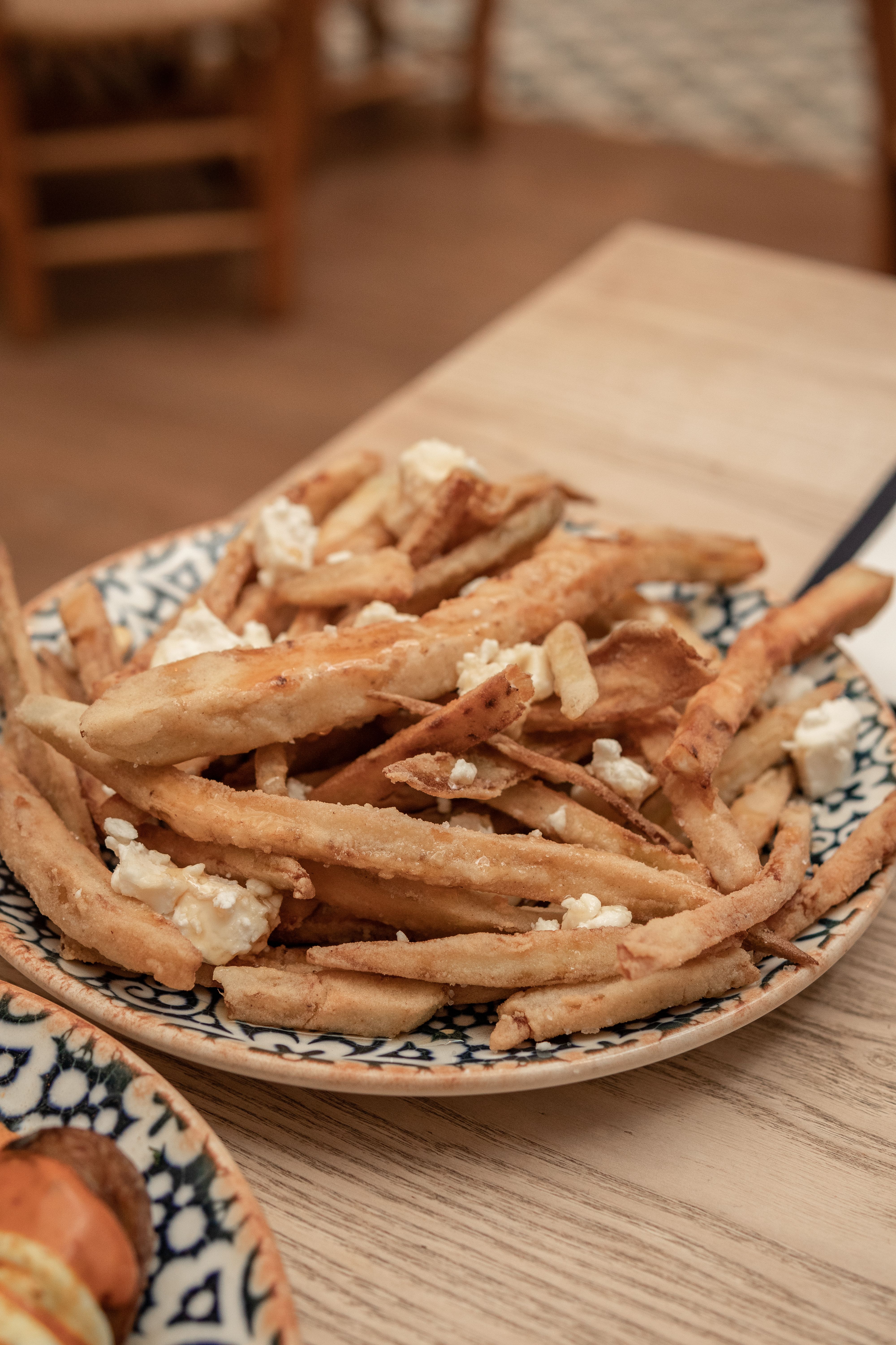 Close-up of rustic fries topped with crumbled cheese served on a decorative plate.