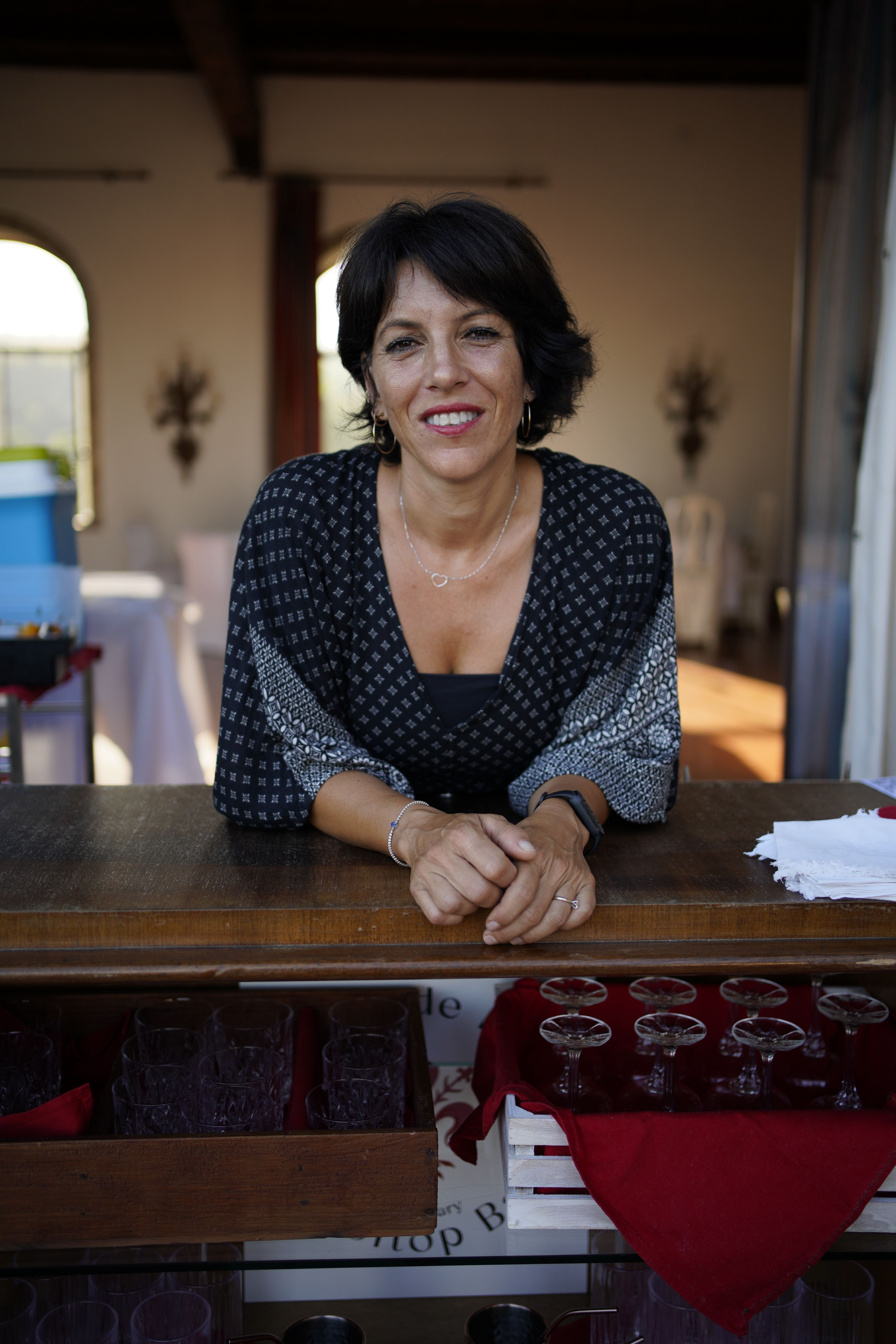 Portrait of a smiling woman standing behind a wooden bar counter in an indoor setting.